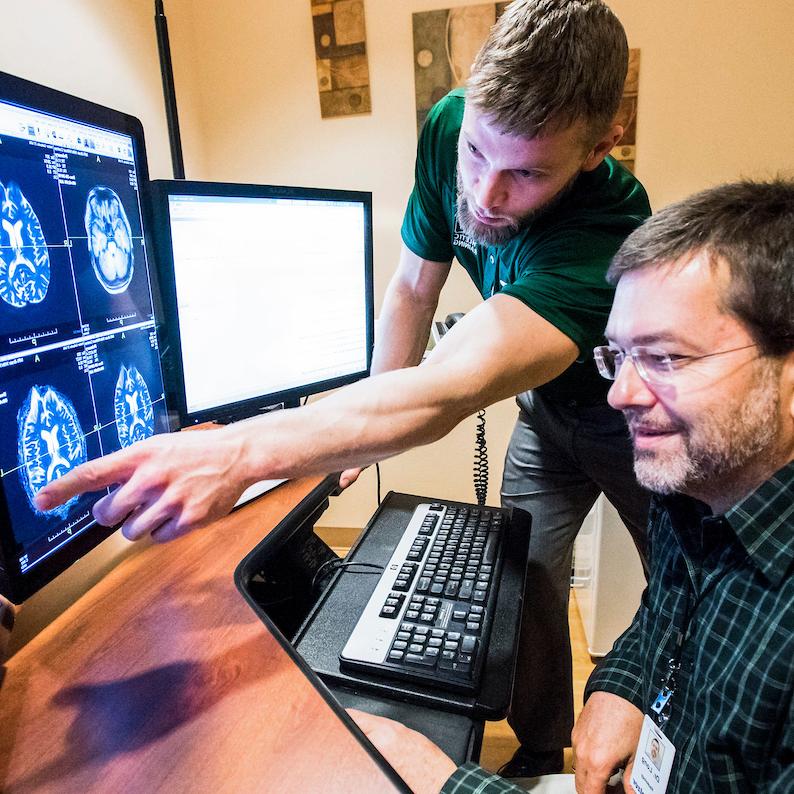 Student points to research on a computer screen with a professor